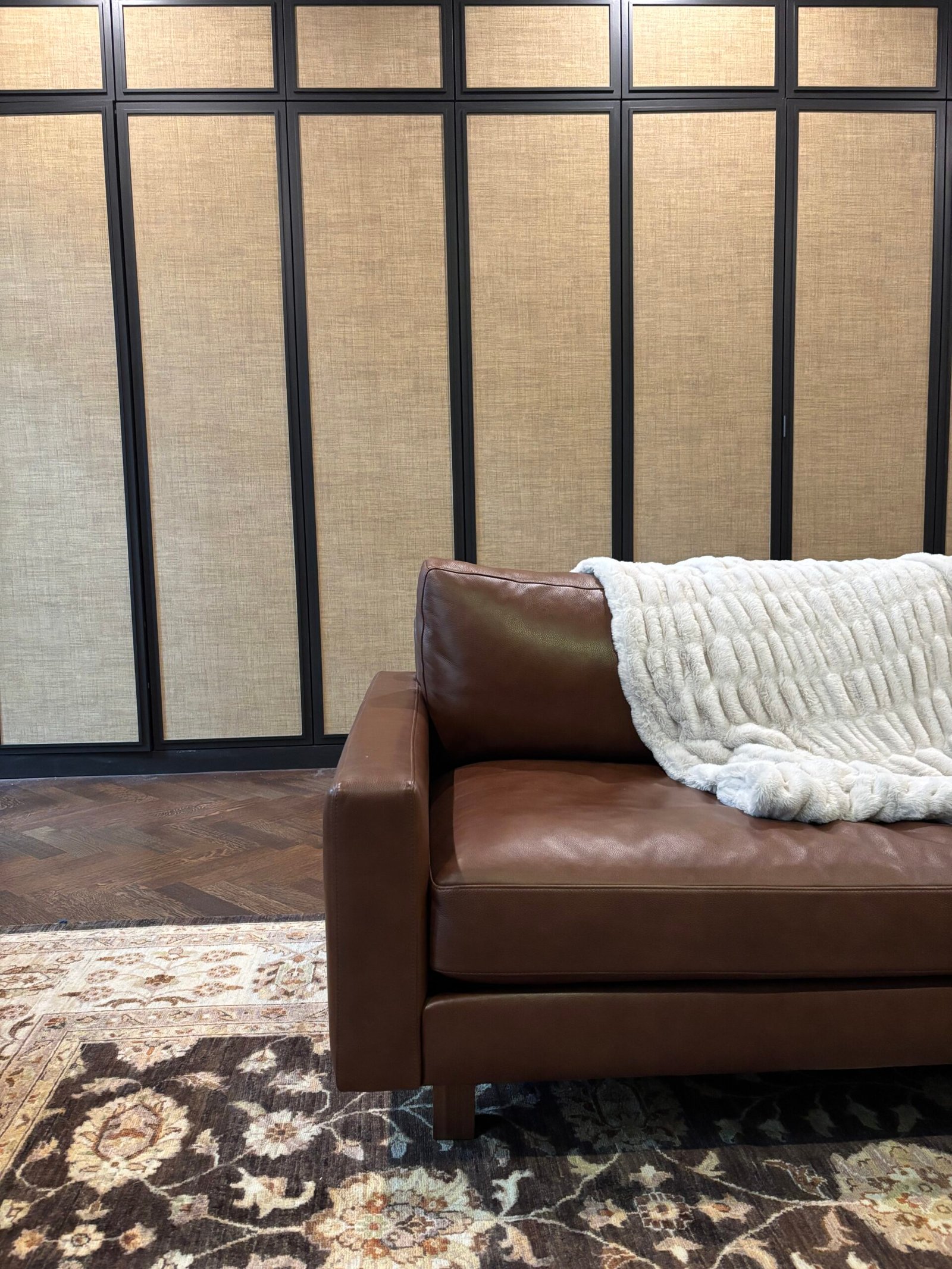 Brown leather sofa placed against a panelled grasscloth wall, NYC