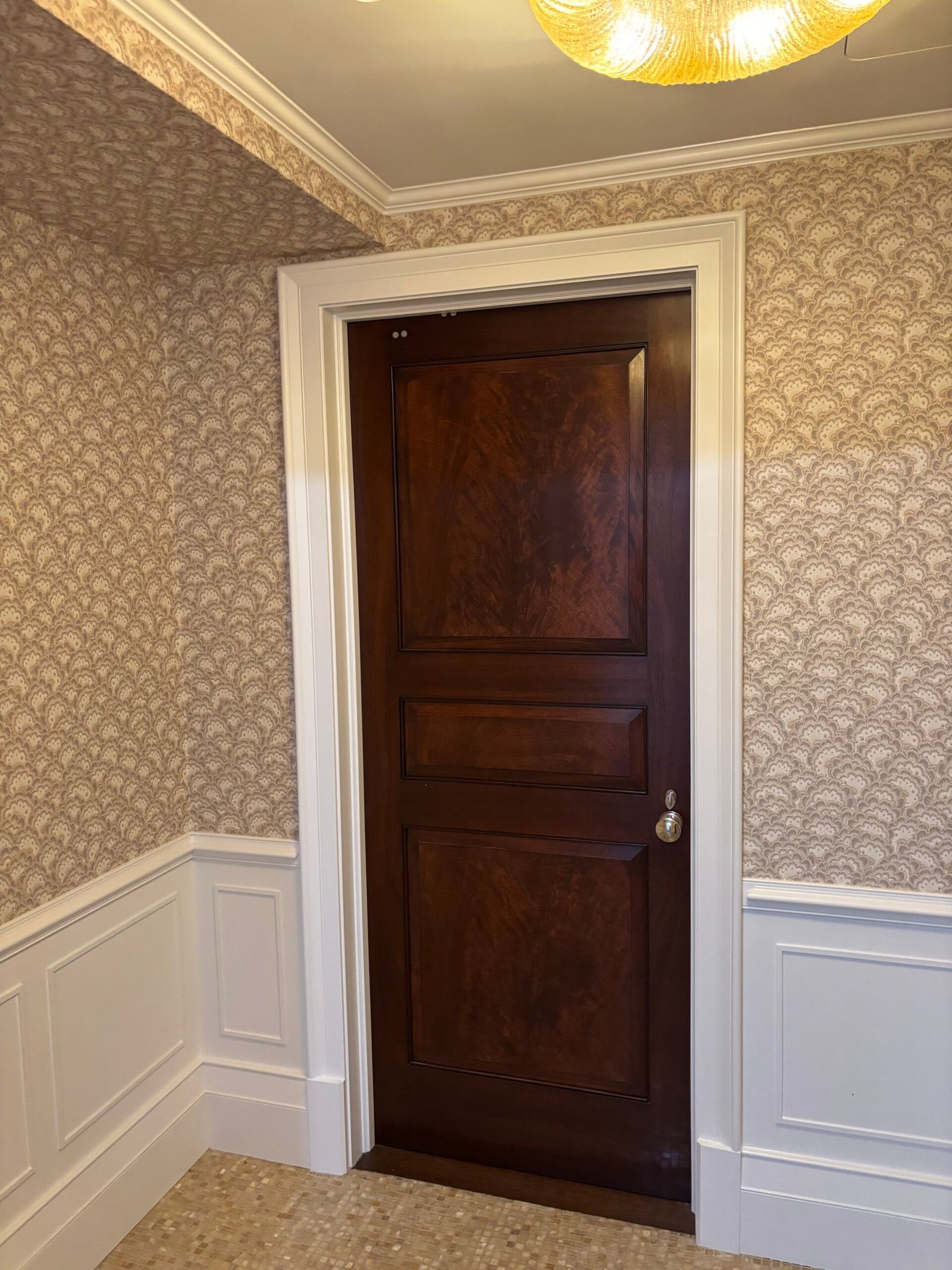 Wood panel door installed in a wallpapered room with wainscoting, NYC