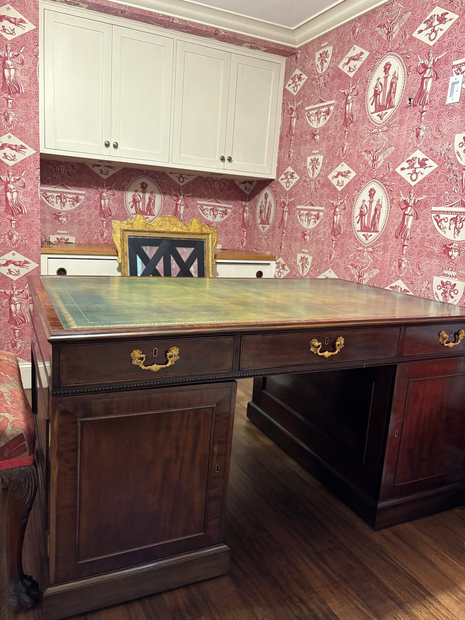 Antique leather-top desk placed in a room with toile wallpaper, NYC